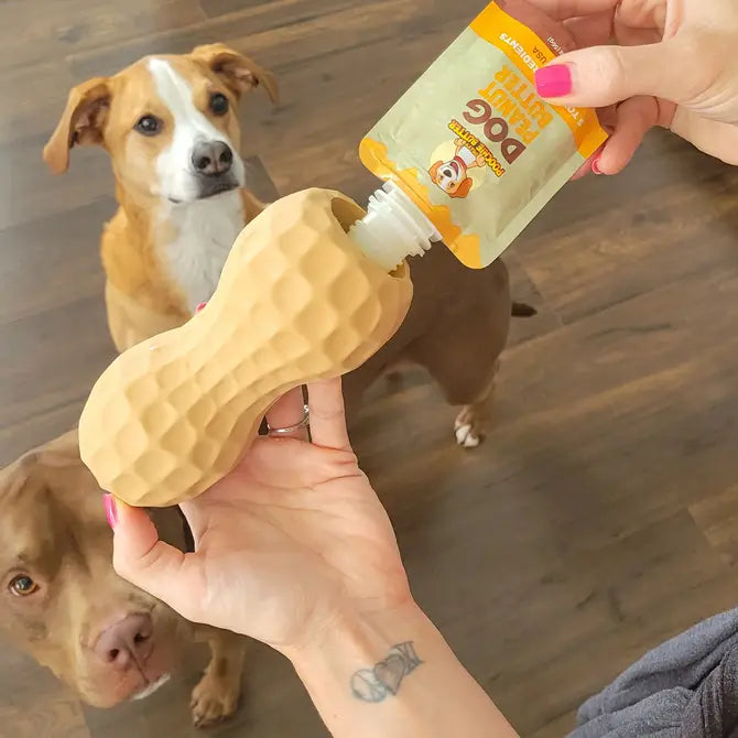 Two cute dogs wait patiently while the squeeze pack is used to fill a peanut shaped toy filler.
