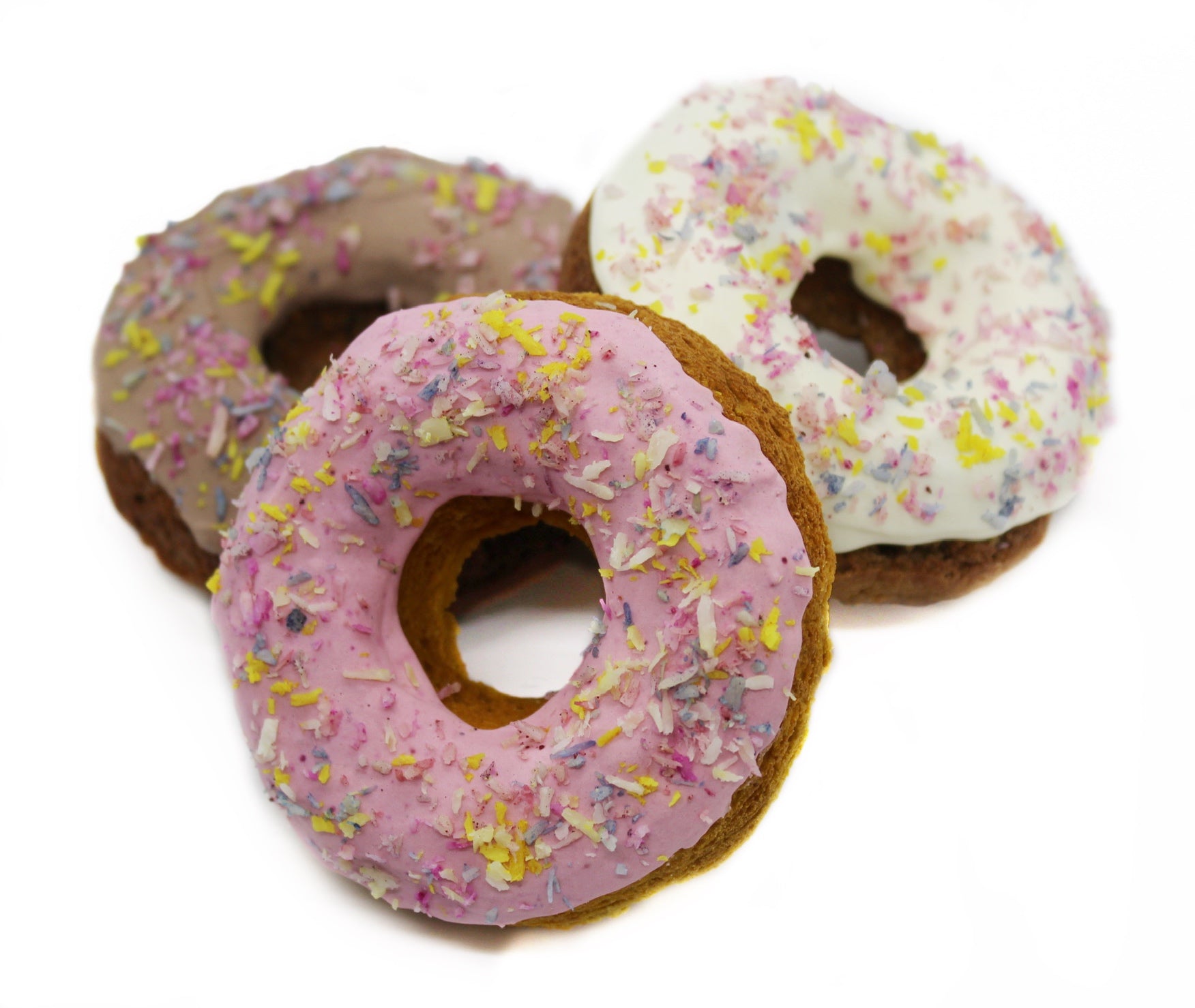 Three Frosted dog donuts with rainbow coconut flakes. Dog donuts are frosted in pink, white, and carob.