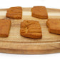A side view of five peanut butter and banana flavored biscuits cut in the shape of the state of Arizona displayed on a wood cutting board. Two of the biscuits have a desert theme stamped on them which shows a moon, mountains, and cactus.