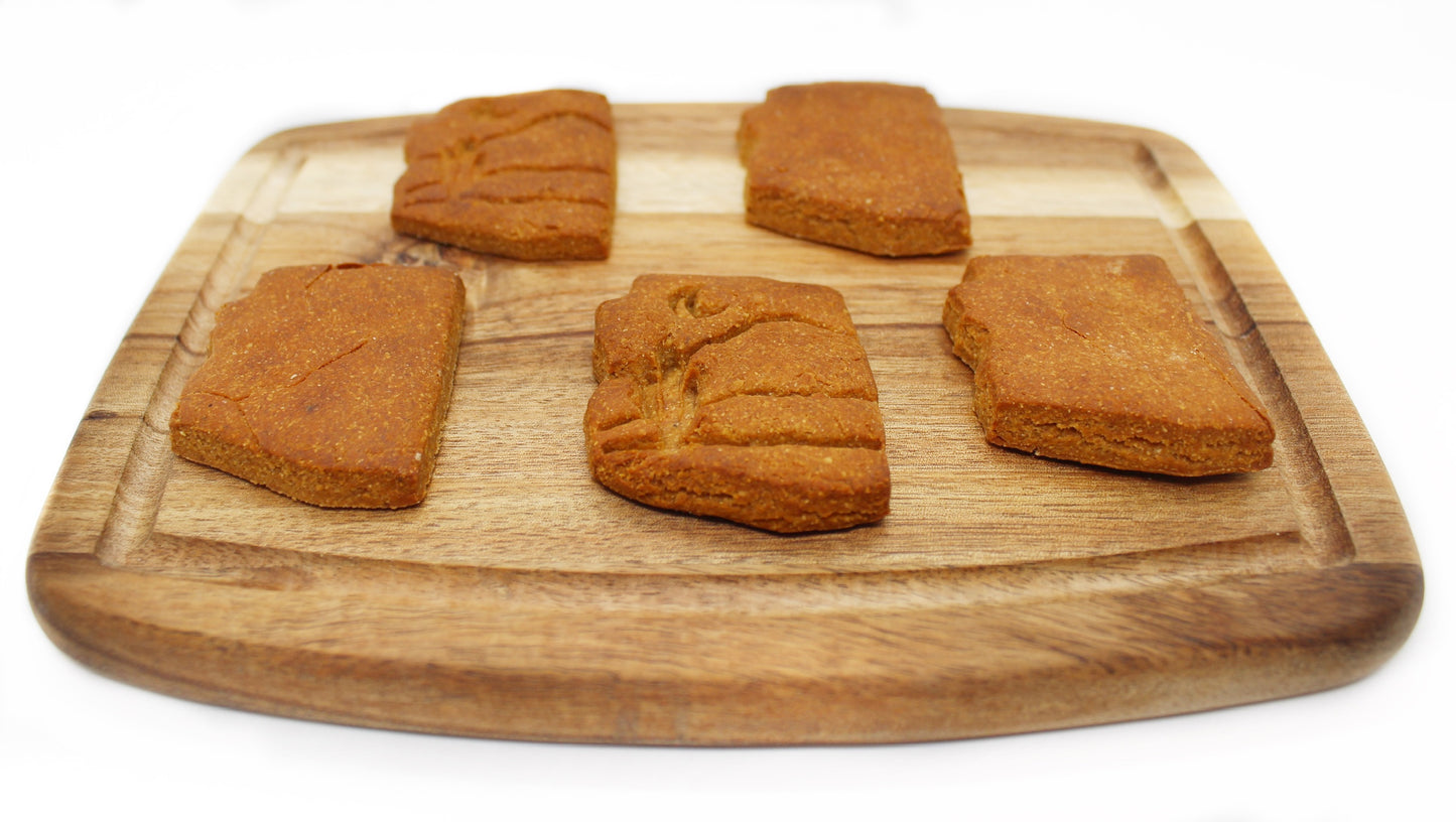 A side view of five peanut butter and banana flavored biscuits cut in the shape of the state of Arizona displayed on a wood cutting board. Two of the biscuits have a desert theme stamped on them which shows a moon, mountains, and cactus.