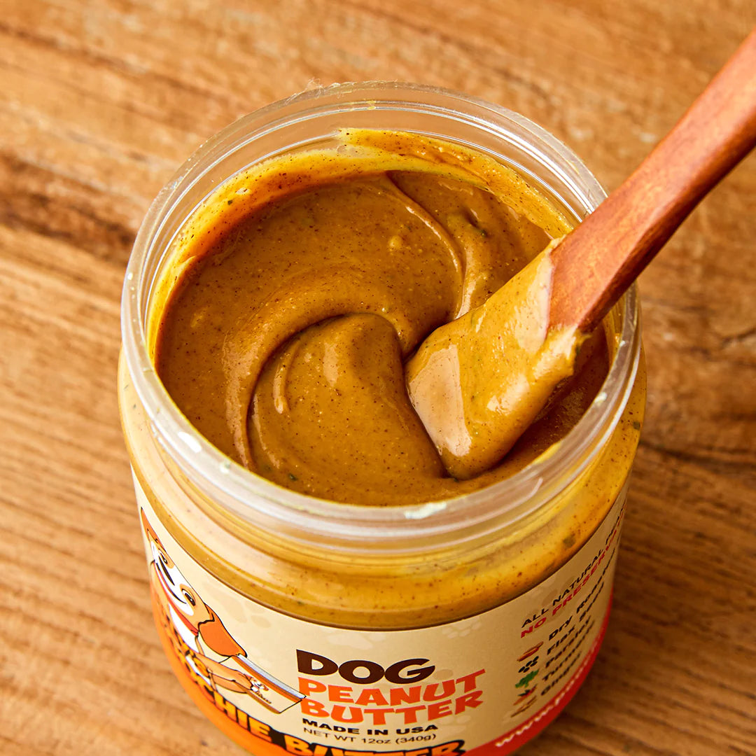 Close up image of the dog safe peanut butter in a jar with a spoon. Showing the texture and coloring of the peanut butter.