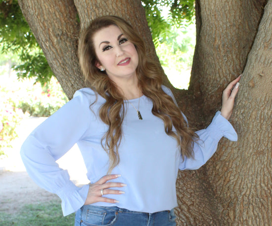 A picture of Kimberly (one of the owner's, the mom) standing by a tree. She's wearing a light blue long sleeve shirt and blue jeans.
