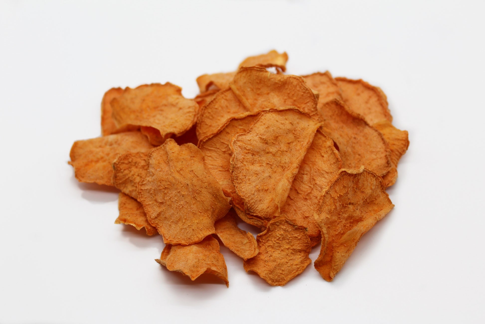 A handful of dehydrated sweet potato chips lightly tossed in cinnamon. The chips are a beautiful bright orange color with flecks of cinnamon.