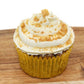 A plump cupcake wrapped in a yellow paper liner with white, piped frosting, crushed peanuts and flaxseed on top.