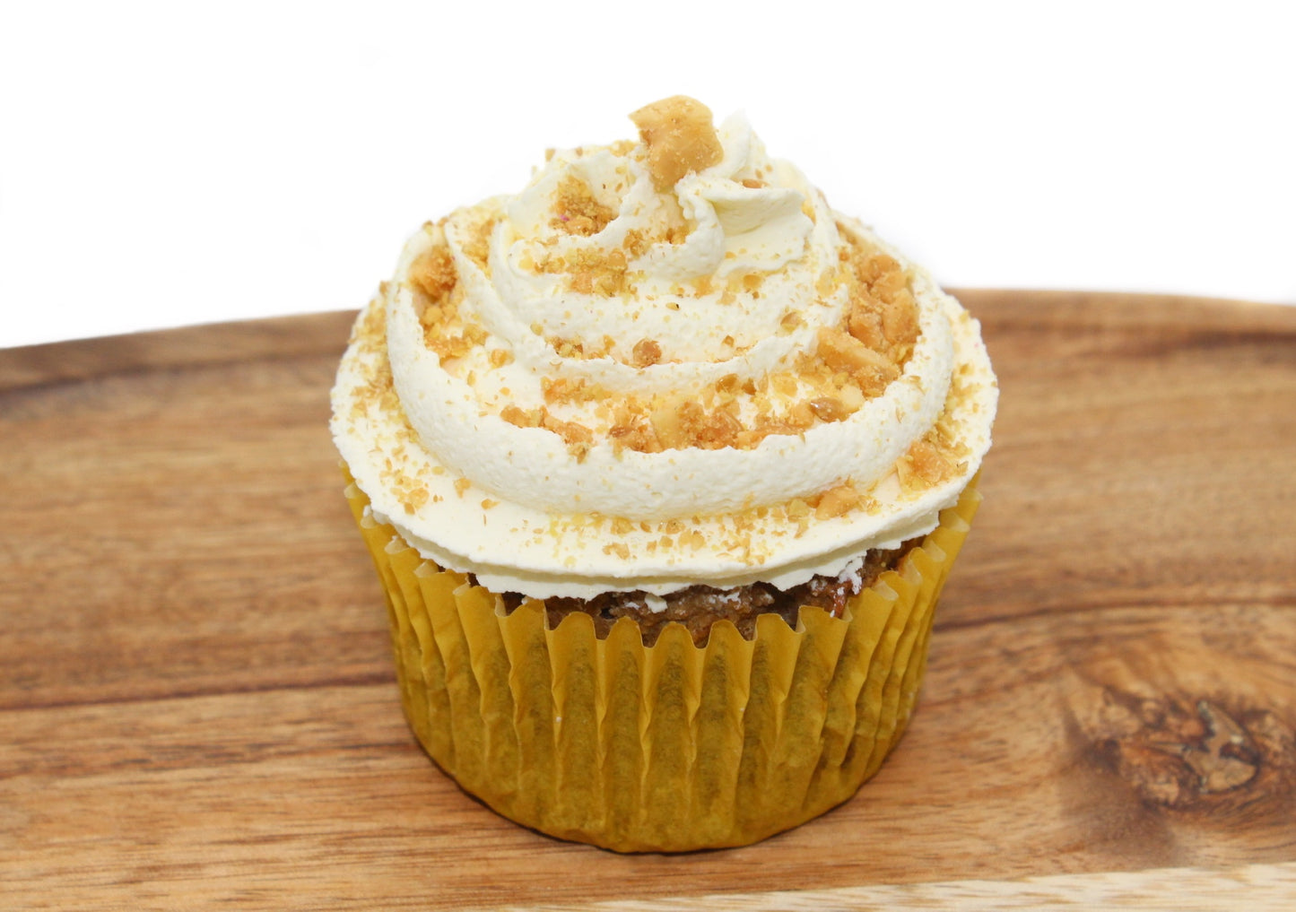 A plump cupcake wrapped in a yellow paper liner with white, piped frosting, crushed peanuts and flaxseed on top.