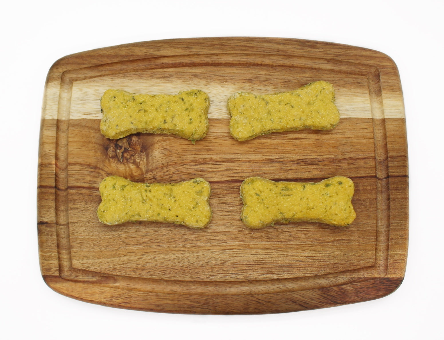 four green bone shaped dog treats on a cutting board in two rows.