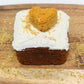 A beautiful sweet potato and carrot flavored mini dog cake with white frosting and flaxseed sprinkled on top. This yummy mini cake also has a heart shaped sweet potato and carrot training treat on top. The mini cake is displayed on a small cutting board with flaxseed sprinkled all around.