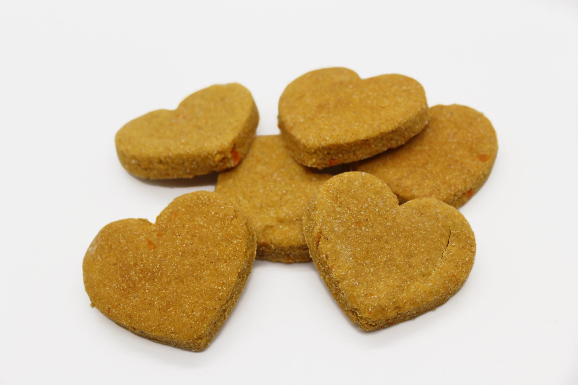 Six sweet potato and carrot flavored dog biscuits all cut in a heart shape. 