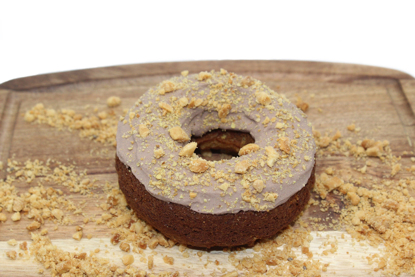 A apple and banana flavored dog donut with brown, carob frosting that has peanuts and flaxseed on top.