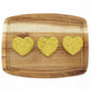 Three green heart shaped dog treats on a cutting board in a line.