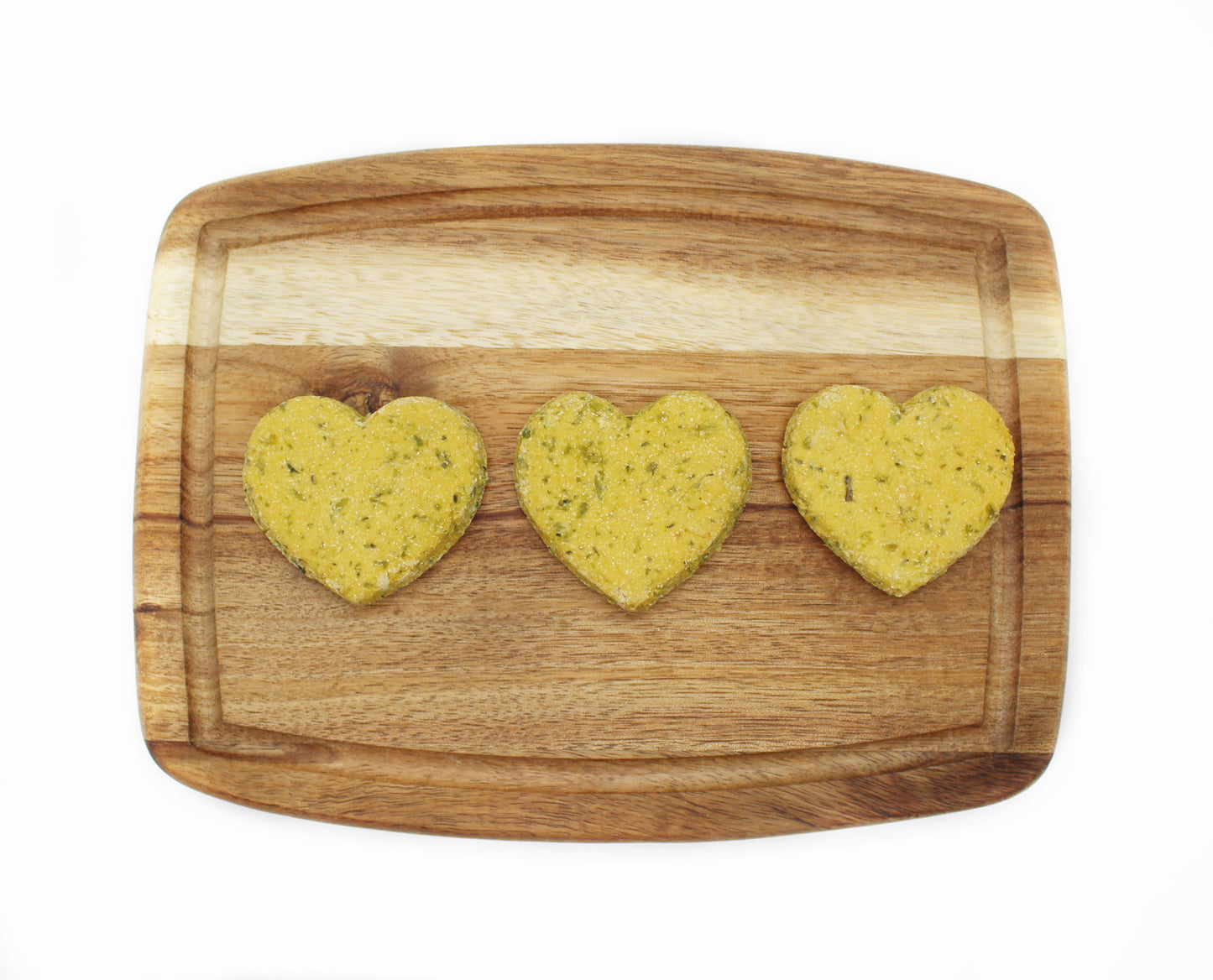 Three green heart shaped dog treats on a cutting board in a line.
