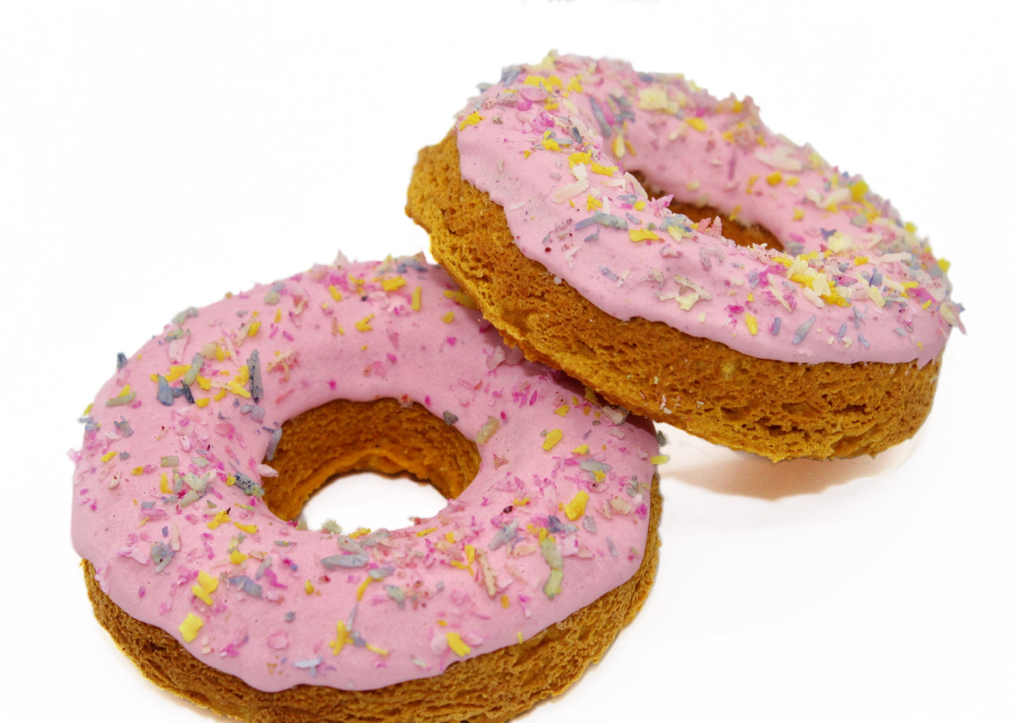 Two pumpkin flavored dog donuts both with pink frosting and  rainbow colored coconut flakes on top.