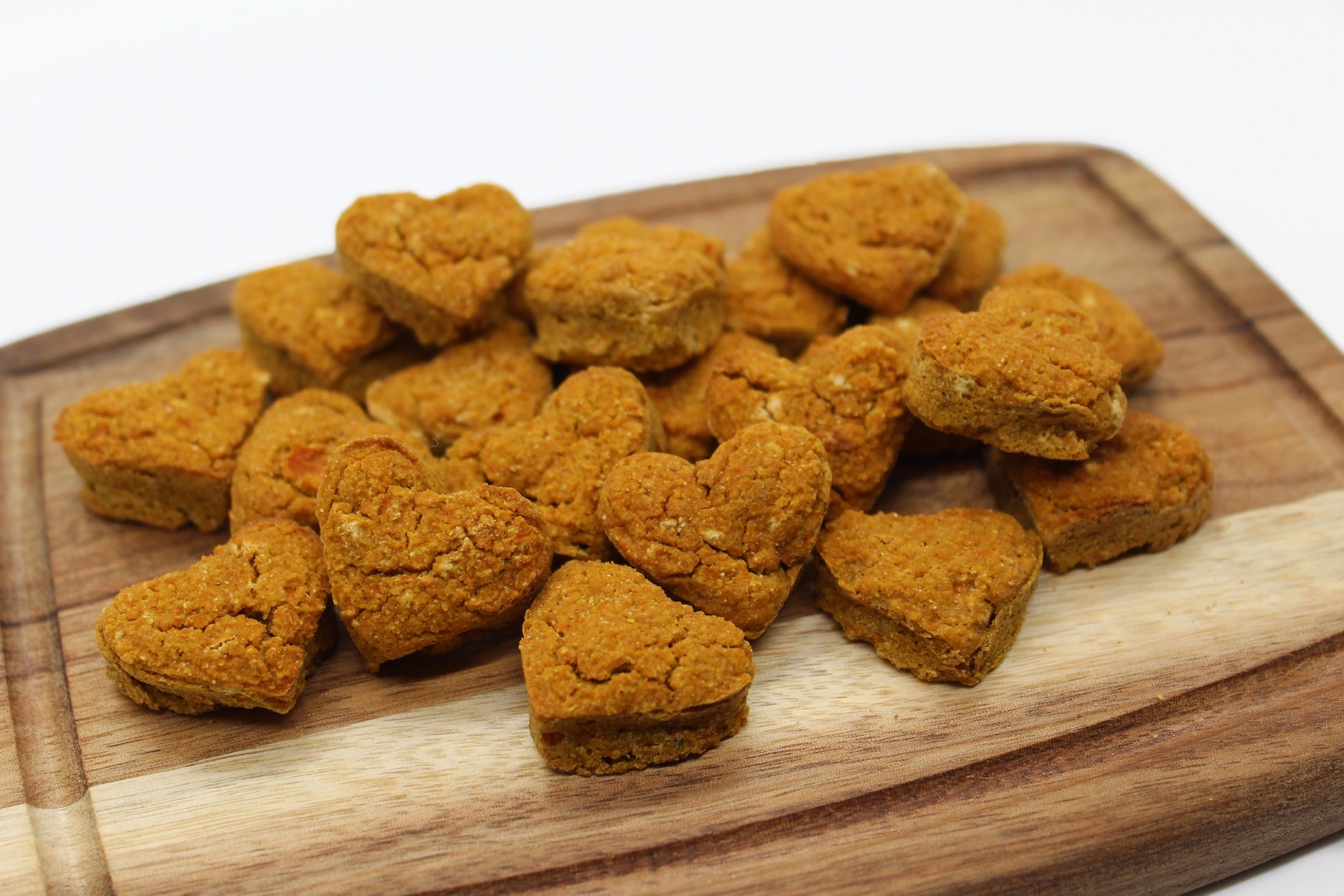 A group of bite-sized, heart-shaped training treats in sweet potato and carrot flavor displayed on a wood cutting board.