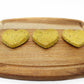 A side view of three green heart shaped dog treats on a cutting board in a line.