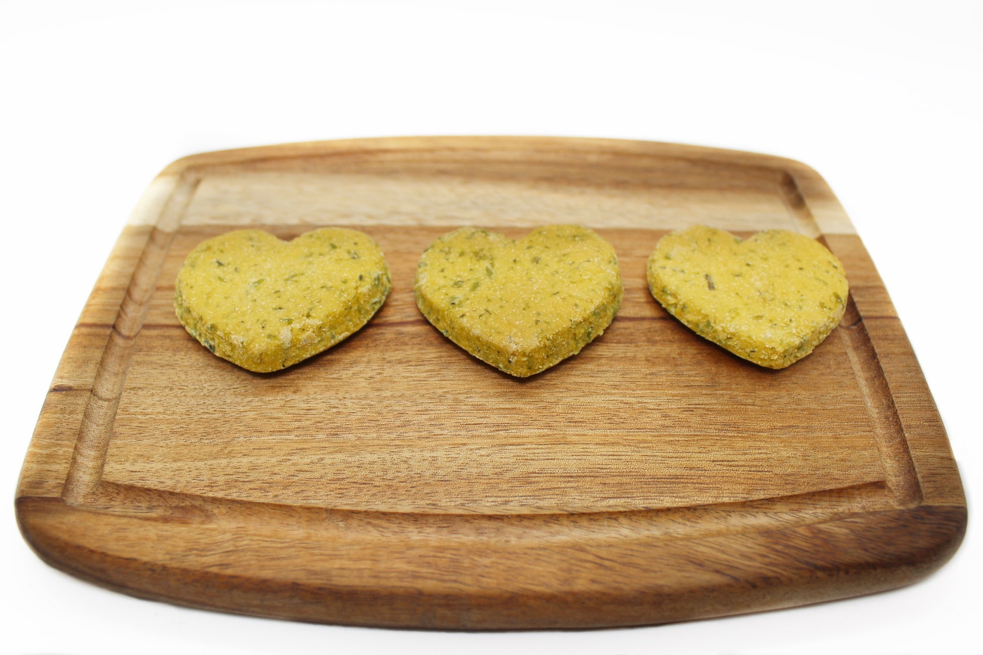 A side view of three green heart shaped dog treats on a cutting board in a line.