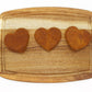 Three heart-shaped peanut butter and banana flavored dog biscuits laid out in a single line on a cutting board.