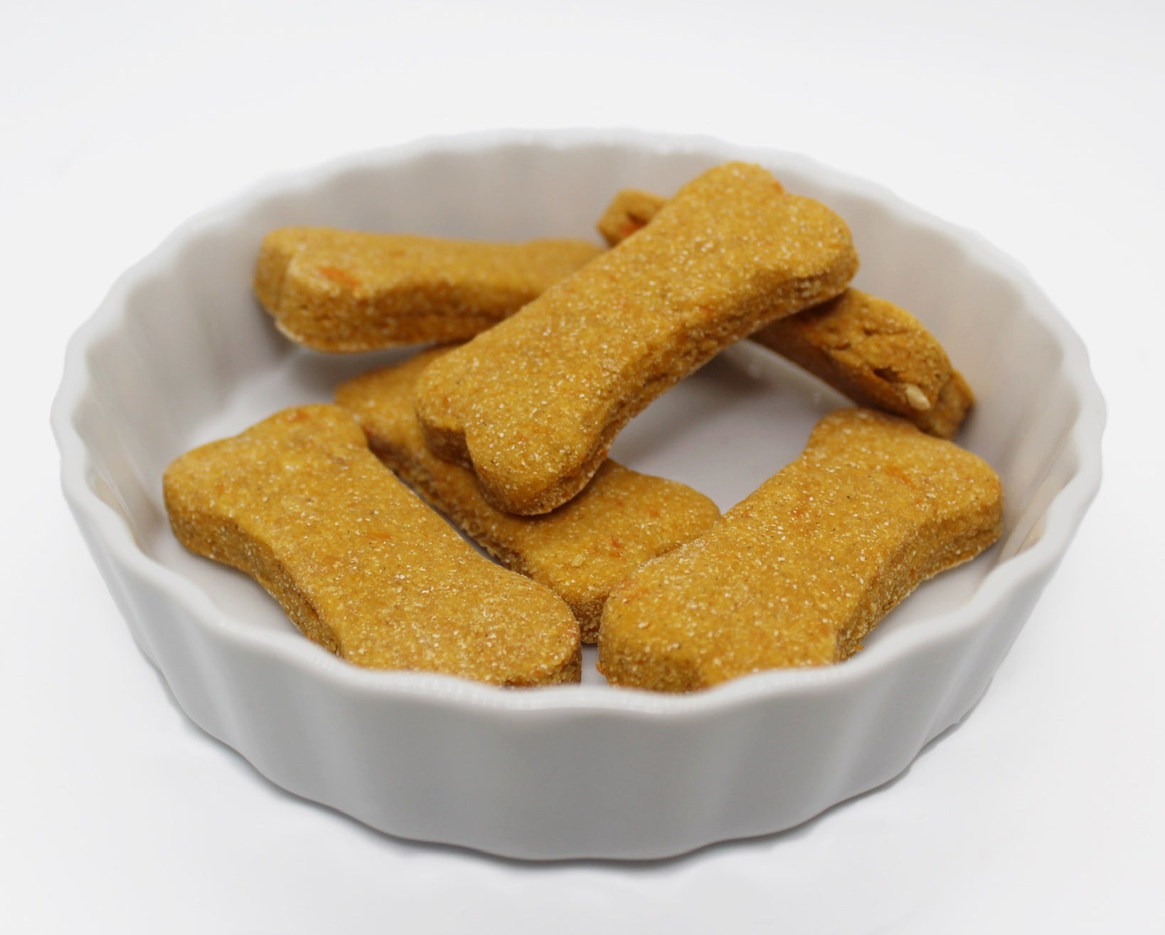 Six sweet potato and carrot flavored dog bisciuts in a small bone shape displayed in a small white dish.