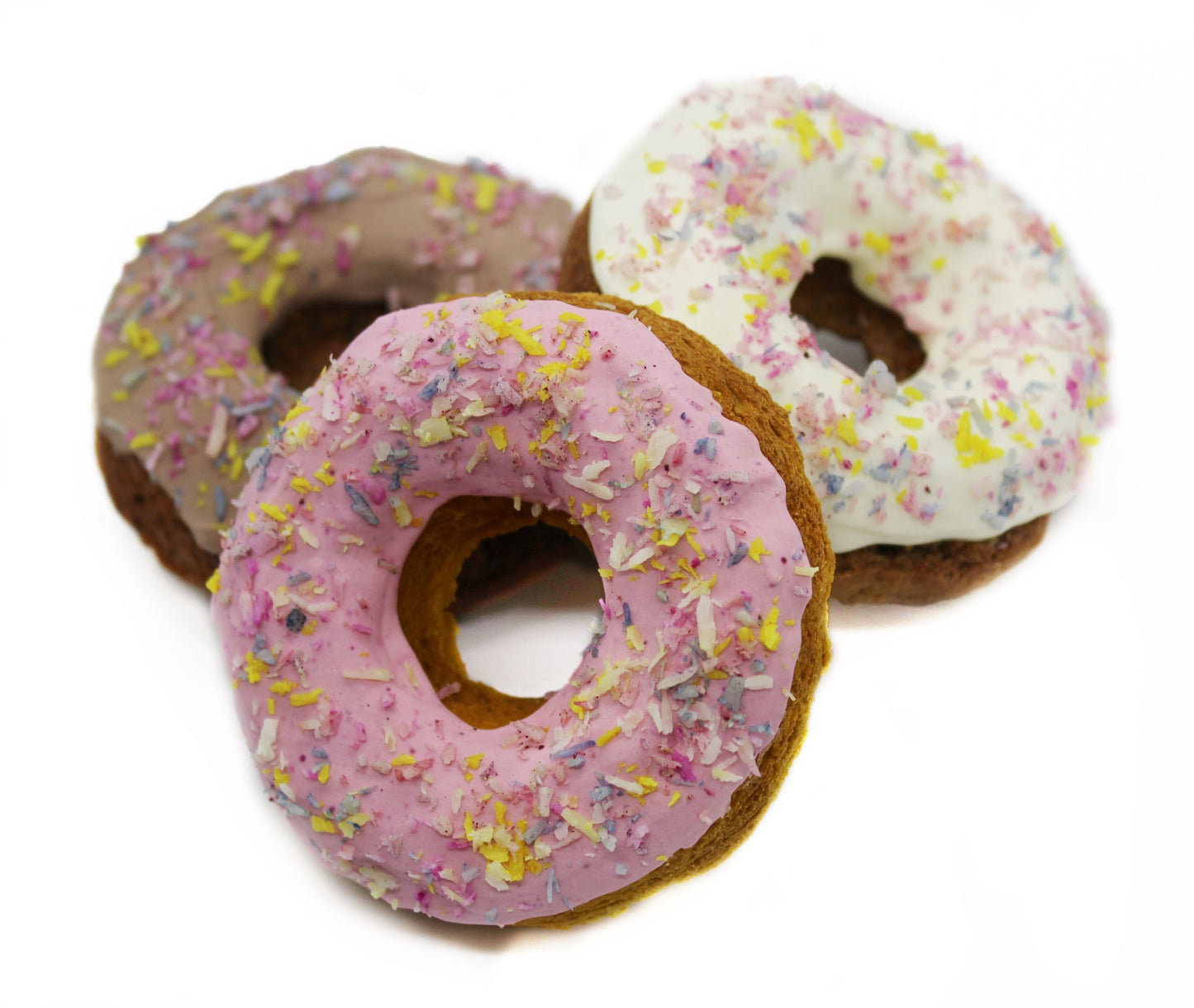 Three Frosted dog donuts with rainbow coconut flakes. Dog donuts are frosted in pink, white, and carob. 
