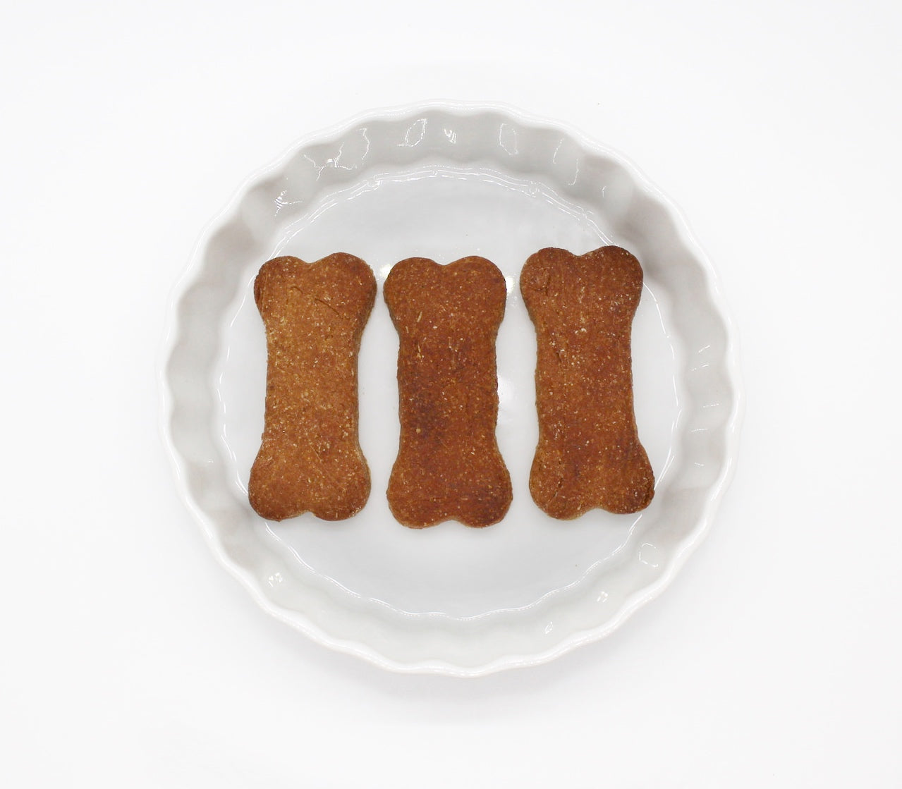 Three bone shaped tasty peanut butter and banana flavor dog biscuits displayed in a round, white dish.