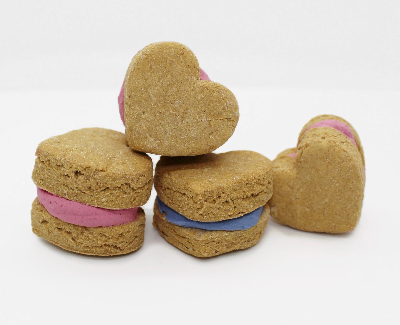 Four apple and banana heart shaped whoopies with dog safe icing in the middle. Three of the whoopies have pink icing in the middle and one has blue icing.